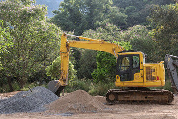 Yellow backhoe with piles of sand and rocks for mixing cement in a forest area for the construction...