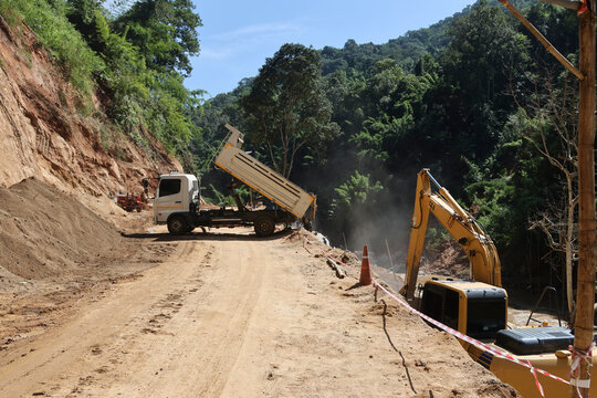 A white truck is dumping sand on the ground on a rural road through a forest being repaired, in the construction area of ​​a road repair contractor.