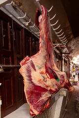 A large, raw side of beef hangs prominently from a metal rail in what appears to be a traditional...