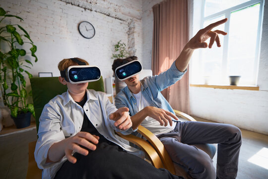 Young family wearing VR headsets are fully immersed in a virtual reality experience in a cozy living room. Concept of modern entertainment at home.