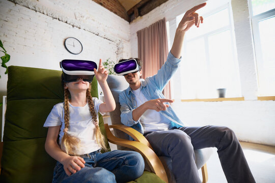 A father and daughter pair engage in exploring virtual reality using a VR headset in a contemporary living room setting. It showcases the idea of family connection through technology and forward
