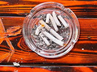 Transparent glass ashtray filled with smoked cigarette butts and ash, placed on vividly colored...