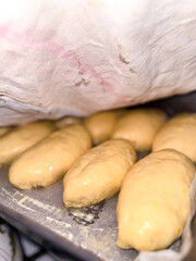 Golden-colored dough portions covered with a cloth, prepared for baking process in a kitchen....