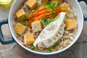 Rice noodles in miso broth with steamed dumpling, smoked tofu and vegetables, middle close-up, horizontal shot