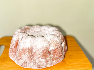 Freshly baked bundt cake lightly dusted with powdered sugar, resting on wooden cutting board....