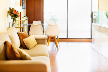 Living room with beige double sofa and brown cushions, natural light and glass table with white chairs