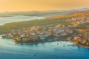Aerial view of the coastal village of Grebastica near Sibenik, Croatia, featuring a deep bay, turquoise Adriatic waters, and lush Mediterranean surroundings in the Dalmatian region