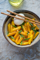 Bowl of korean tteokbokki or rice cakes with curry sauce and boiled egg, vertical shot, elevated view