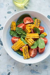 Plate with tomato, fresh spinach and grilled corn salad, vertical shot on a white and blue granite background, high angle view