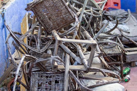 A large, chaotic pile of weathered and broken wicker furniture and chair components lies discarded against a distressed blue wall, highlighting urban deca