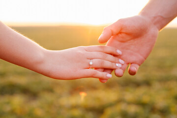 Loving couple holding hands at sunset in a field, showing engagement ring