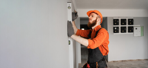 construction foreman using spirit level on concrete wall. Repairman wearing blue coveralls at...