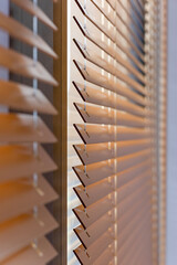 Close-up side view of wood blinds, capturing the angled slats as they filter sunlight. Made from natural materials, these blinds offer stylish light control and remain cool under direct sun. Not AI.