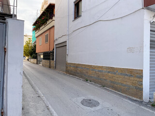 Everyday scene from Albania: quiet road, small homes, electrical wires, and bushes. Realistic and...