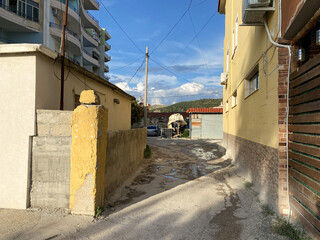 Obraz premium Typical day in a local Albanian neighborhood: old rooftops, narrow road, utility poles, and surrounding plants. The kind of everyday setting that quietly speaks of tradition and time.