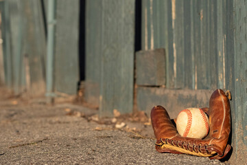 Outdoor baseball and mitt resting against a green wooden fence. Shot in the evening for long shadows. Vintage and rustic to invoke childhood memories. 58mm. I left lots of copy space.