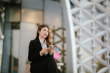 Fototapeta premium Businesswoman in black suit holding laptop and smartphone smiling confidently outdoors in modern urban environment