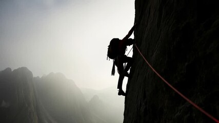 Man Climbing Steep Rock Face with Gear in Misty Mountains - Powered by Adobe