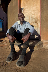 village single african man sited in front of the house in the yard, sunny day