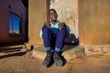 village single african school boy sited in front of the house wearing uniform