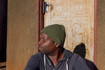 village single african man sited in front of the house in the yard, sunny day
