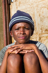 village single african boy sited in front of the house , in the yard, sunny day,