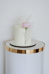 Minimalist white cake adorned with a delicate pink flower and artistic translucent elements.