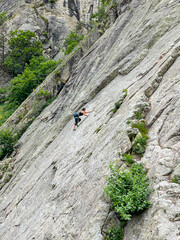 Experienced female climber ascending on a steep, rough rock face. Challenging nature of sport...