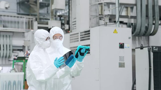 Male and female workers in protective clothing inspecting silicon wafers with tablets in a semiconductor factory