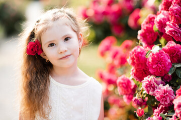 Smiling cute blonde child girl 4-5 year old with rose flowers outdoors. Summer season. Childhood.