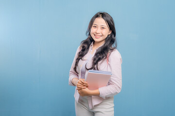 Fototapeta premium A woman is holding a book and a backpack. She is smiling and looking at the camera. Concept of confidence and readiness, as the woman is prepared for her day ahead