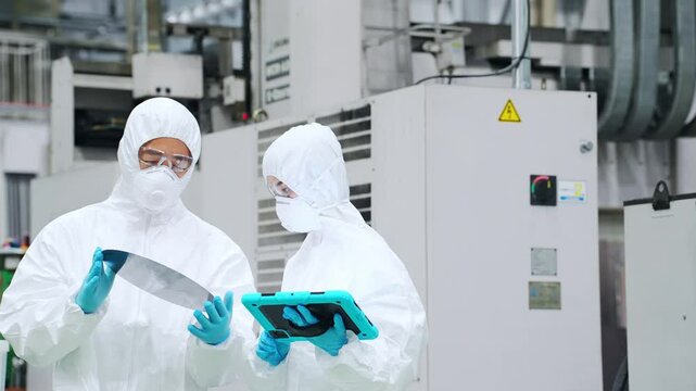 半導体工場でタブレットを持ってシリコンウエハーを検査する防護服を着た男女作業員