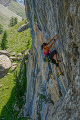Athletic woman is intensely focused on her ascent up a steep rock wall, her body positioned for the...