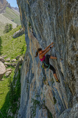Strong, agile woman caught in the middle of climbing an overhanging rock face, demonstrating...