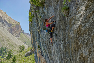 Woman in a pink top and black leggings actively climbs a textured rock face, reaching for a...