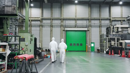 Male and female workers wearing protective clothing walking in a factory.