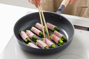 フライパンでアスパラベーコンを焼く料理のシーン　Asparagus Bacon Being Cooked in a Frying Pan