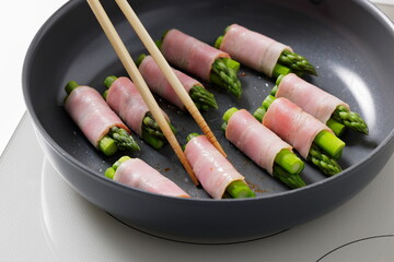 フライパンでアスパラベーコンを焼く料理のシーン　Asparagus Bacon Being Cooked in a Frying Pan