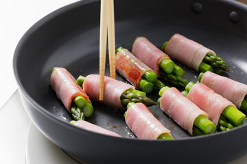 フライパンでアスパラベーコンを焼く料理のシーン　Asparagus Bacon Being Cooked in a Frying Pan