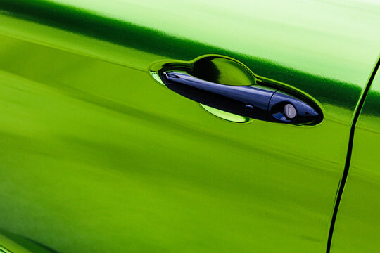 A vibrant, close-up shot of a sleek black car door handle against a striking metallic green car body