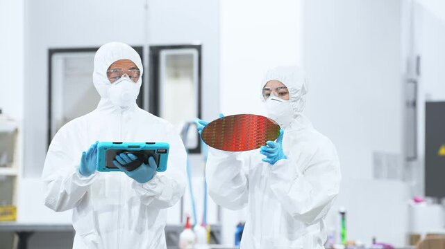 半導体工場でタブレットを持ってシリコンウエハーを検査する防護服を着た男女作業員