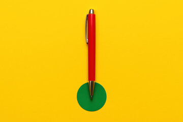A vibrant red pen placed precisely on a green circular cutout against a bright yellow background highlights focus and clarity in business creativity