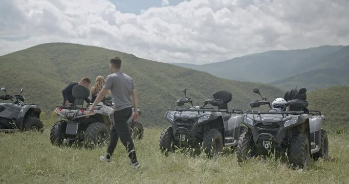 Friends enjoy a quad bike adventure in the mountains. They take a break to admire the beautiful view and prepare for the next leg of their journey.