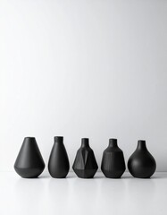 minimalist matte pale modern black vases of various shapes lined up on a white background
