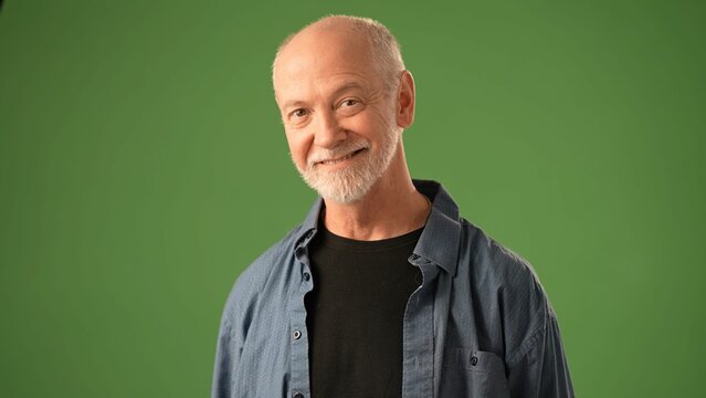 A mature man with a thoughtful boring expression stands against a solid green screen background. His hands are clasped, indicating deep contemplation or reflection.