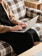 Person typing on a laptop while seated on a plaid sofa