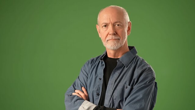 A senior man with a warm smile stands in front of a solid green screen. He wears a black shirt and a blue jacket, showcasing a friendly and approachable nature. - Powered by Adobe