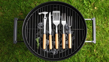 A top-down view of a barbecue grill with cooking utensils arranged neatly on grass