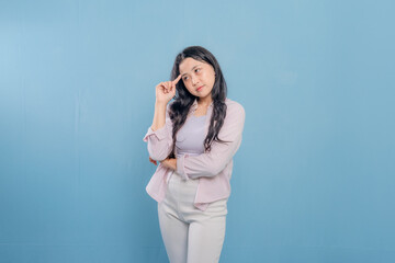 A woman is standing in front of a blue wall, wearing a pink jacket and white pants. She is looking...