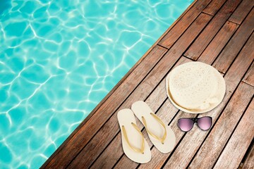 Hat and flip-flop with sunglasses by swimming pool